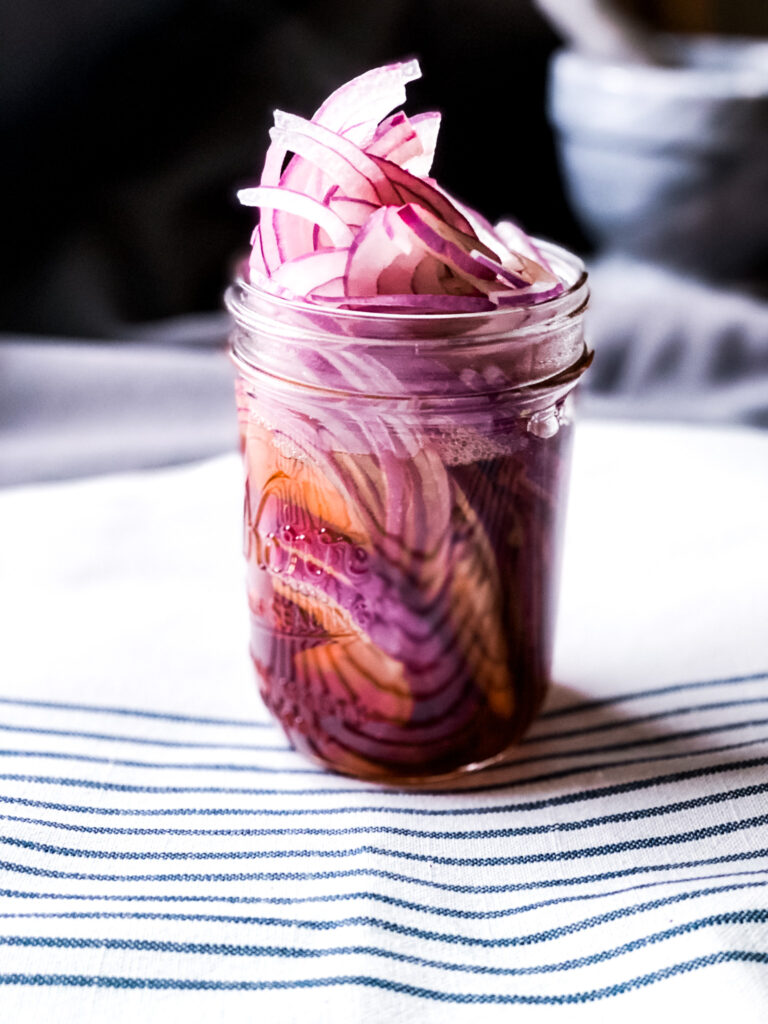 Pickled Red Onion in glass jar on white striped table cloth
